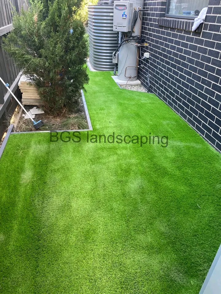 Narrow side passage beside a dark brick wall, covered in artificial grass, installed by BGS Landscaping