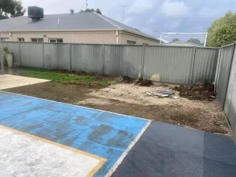 Bare soil and sand beside a blue-painted concrete patch and dark paving, seen from another angle