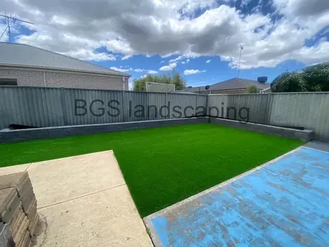 Artificial grass with a dark block edge along the fence, a pale concrete area at the left and the blue-painted patch at the right