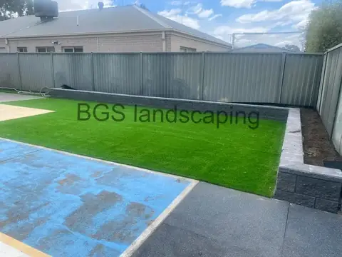 Artificial grass with a block wall that steps up at the right, and the blue-painted concrete patch at the bottom left