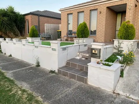 White rendered low wall with grey tiled steps, planters with small conifers and a letterbox in front of a tan brick house