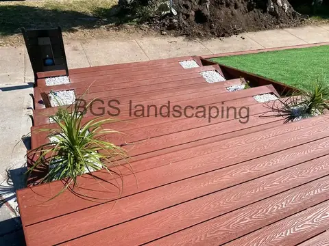 Red-brown deck boards with a wood-grain texture, a plant in a deck planter and artificial grass at the top right
