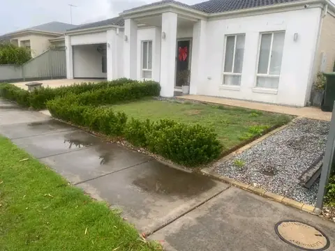 Hedge, lawn and gravel beside a wet concrete path, seen from another angle in front of a white house