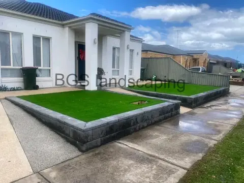 Raised dark grey block bed with artificial grass in front of a white house