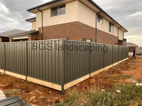 Dark grey sheet-metal fence with a timber board along the bottom, in front of a two-storey brick house