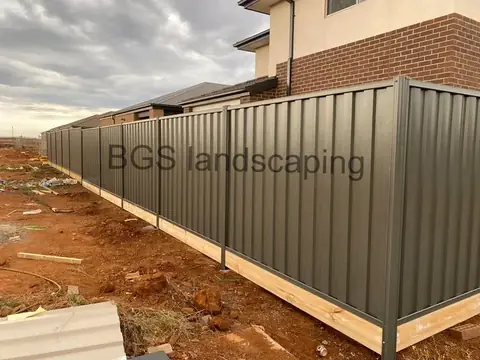 Long run of dark grey metal fence with a timber board along the bottom, on cleared reddish soil