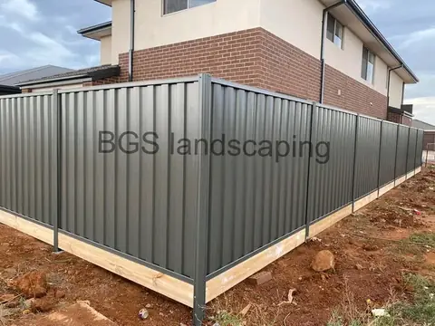 Dark grey metal fence with a timber board along the bottom beside a brick house