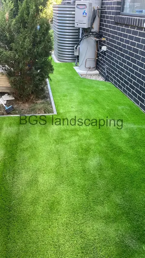 Narrow side passage covered in artificial grass beside a dark brick wall