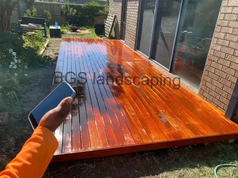 Glossy reddish-brown timber deck seen from another angle, with sliding glass doors and a garden at the back