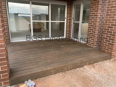 Dark stained timber deck against sliding glass doors, beside a brick pillar