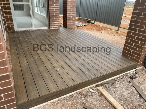 Dark stained timber deck in a brick corner, with a grey metal fence in the background